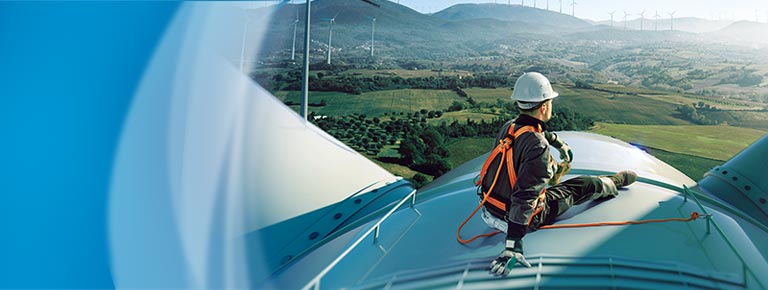 A man wearing working gear and sitting on top of a wind turbine